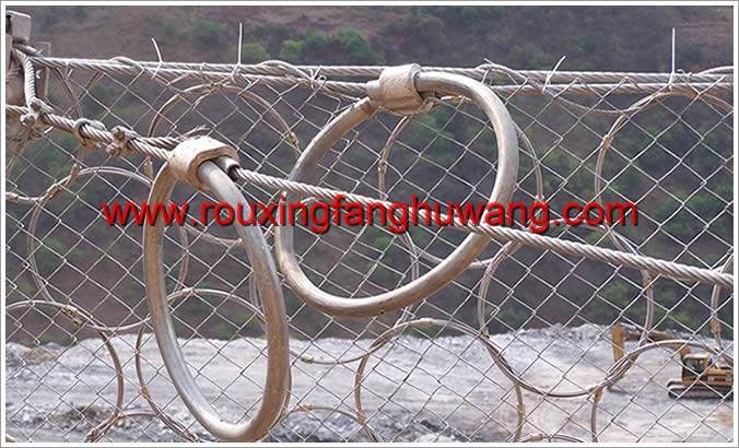 安装着环形被动防护网的远处的山脚下一台挖掘机正在施工