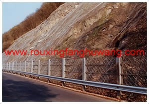 公路一侧的山脚下由混凝土浇筑的基柱的波形护栏板的上面安装着落石防护网