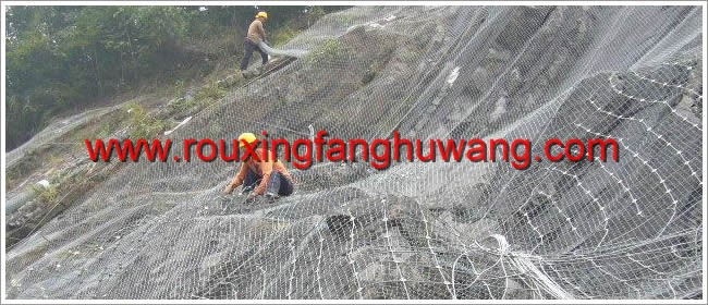 在边坡上一个工人正在从上往下铺着钢丝隔栅另一个施工人员在一旁用缝合绳缝合主动防护网的钢丝绳网